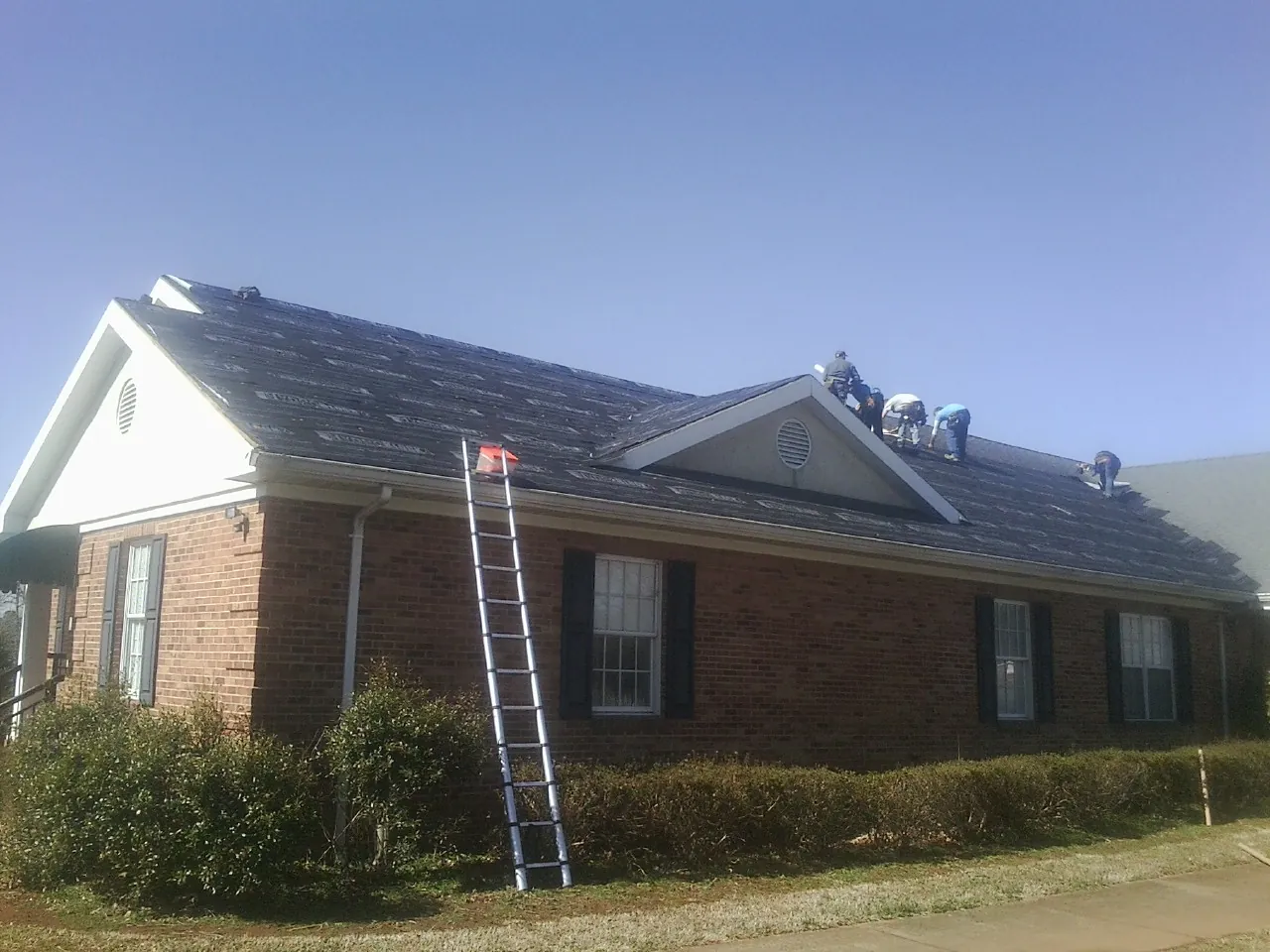 Crew tearing shingles off a brick ranch roof with a ladder set — Emergency Roof Repair work by our crew in Ellendale