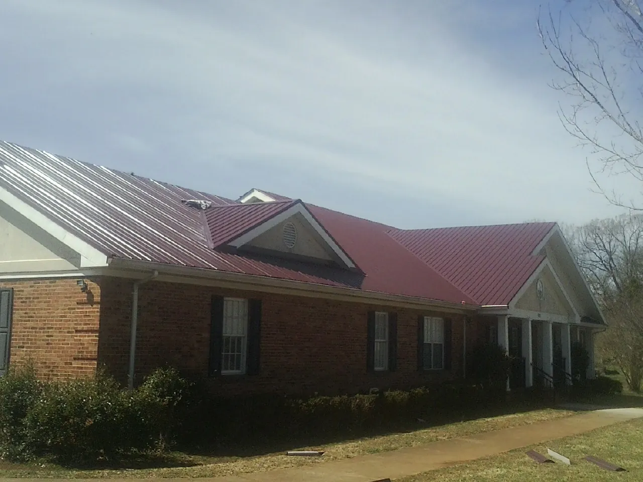 Red metal roof with gabled entries on a long brick building, from a Hail Damage Roof Repair job in Ellendale