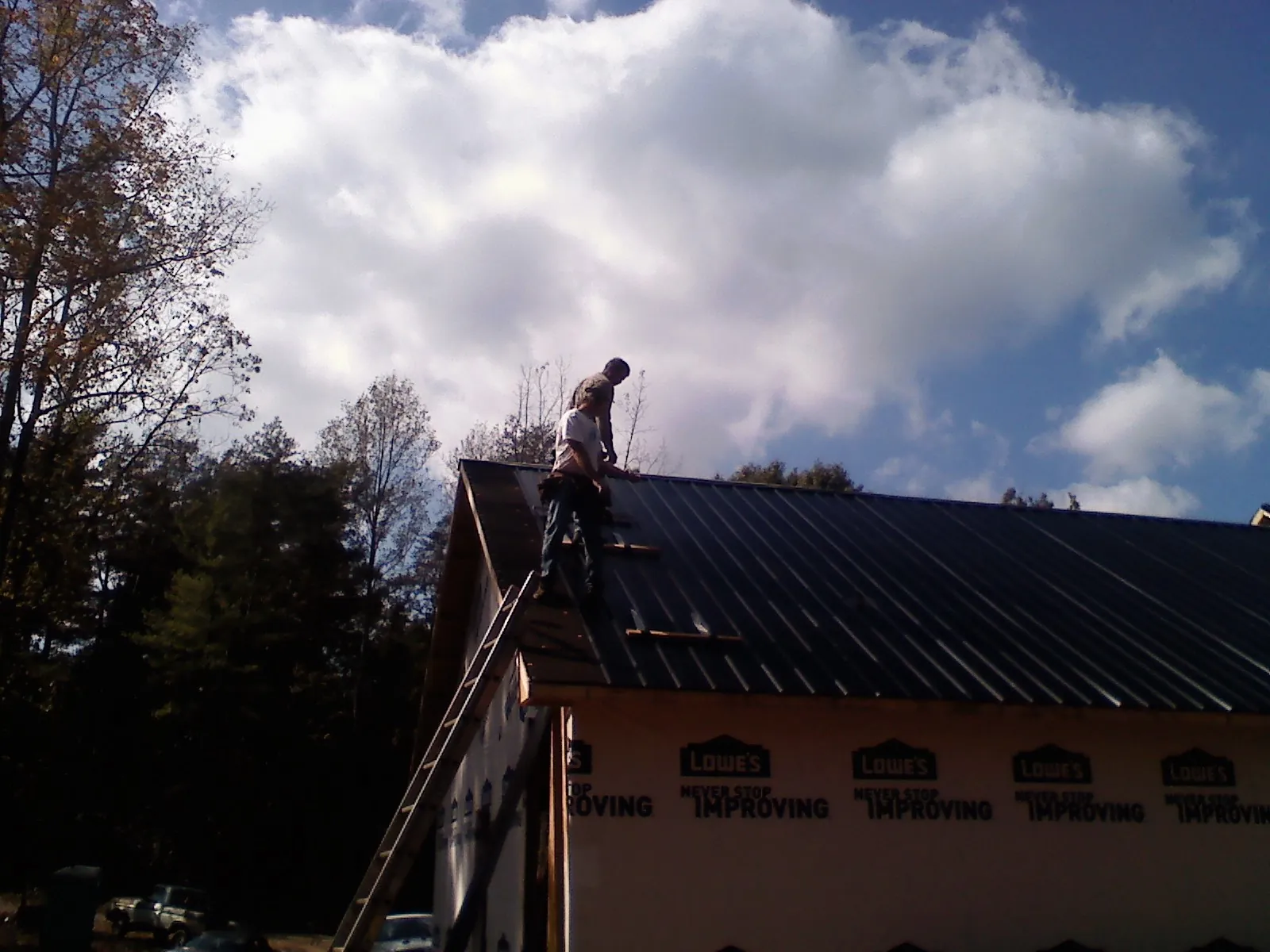 Roofer fastening dark metal panels high against a cloudy sky, from a Roof Inspection job in Ellendale